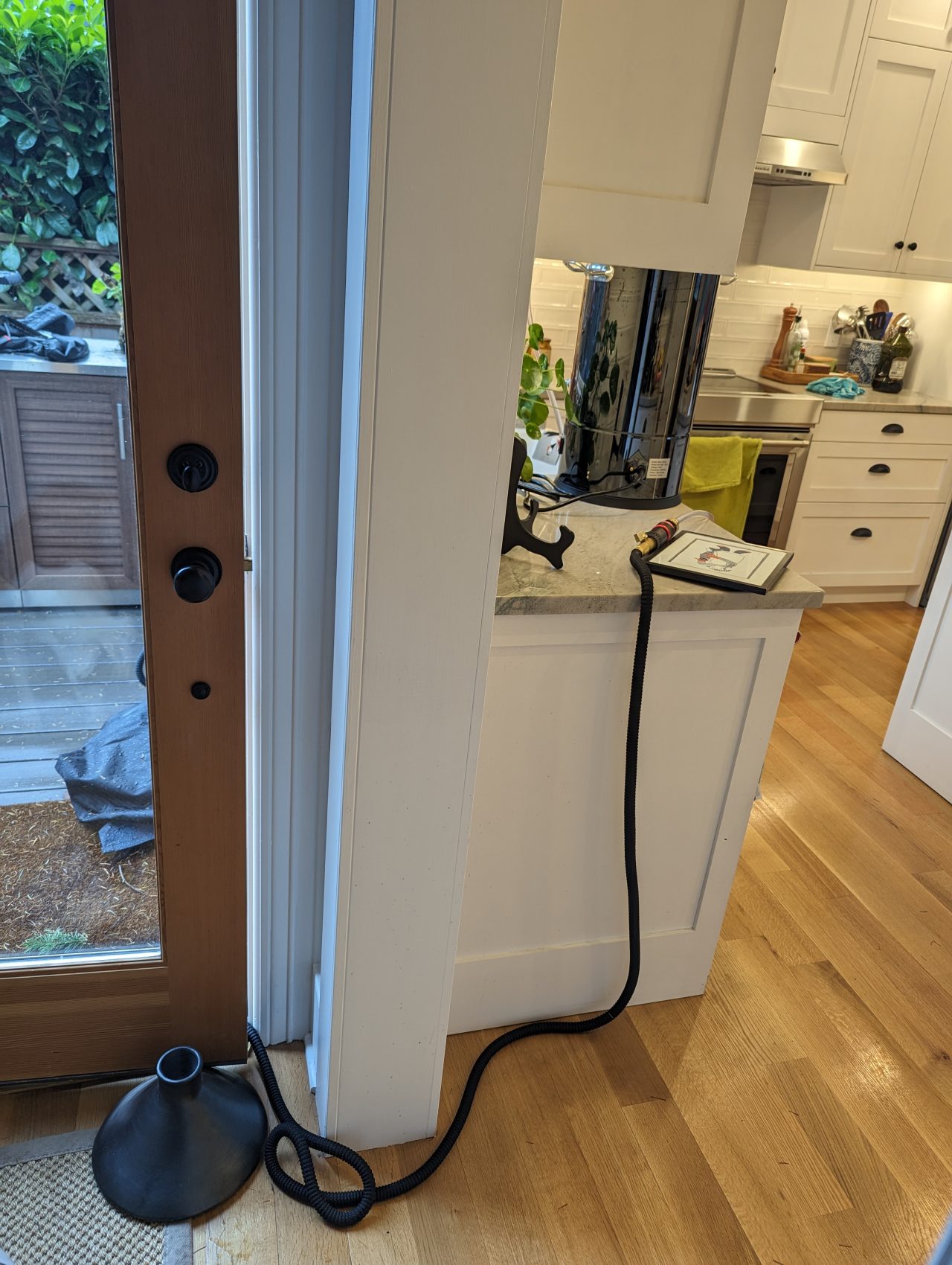 Photo of a garden hose running through an open door and up to a wort chiller in a brewing kettle
