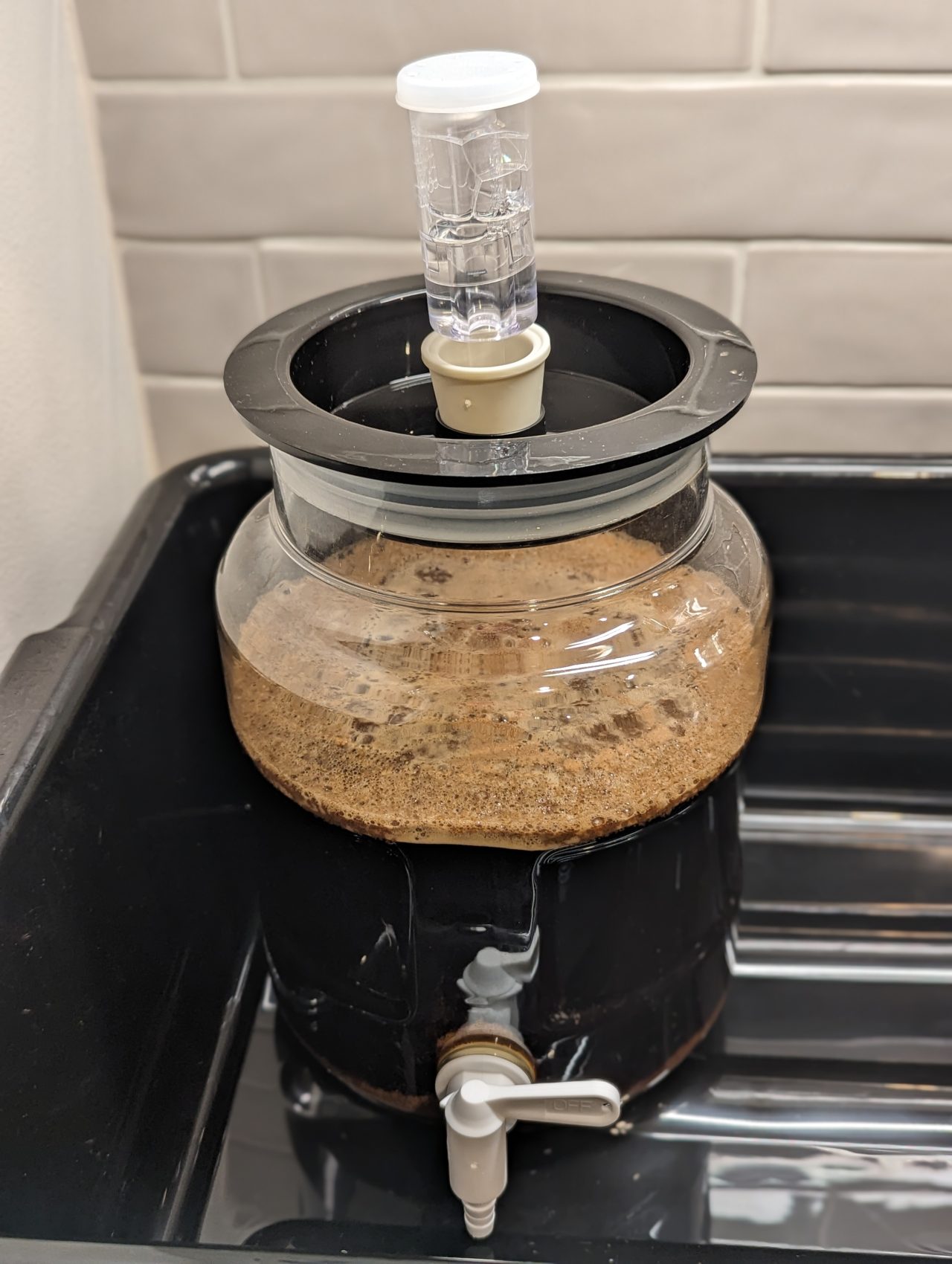Photo of a batch of stout beer in a one-gallon fermenter with foam on top