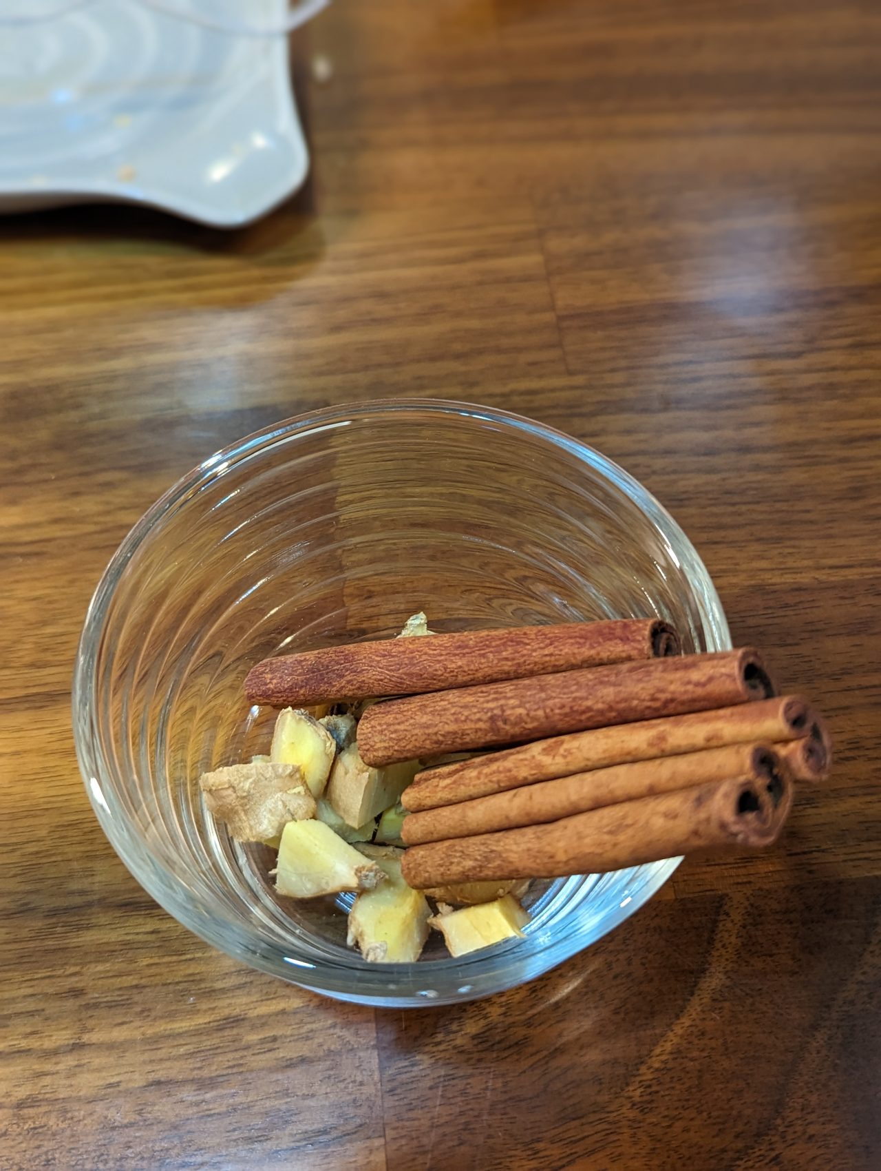 Photo of cinnamon sticks and chunks of ginger root in a small glass bowl