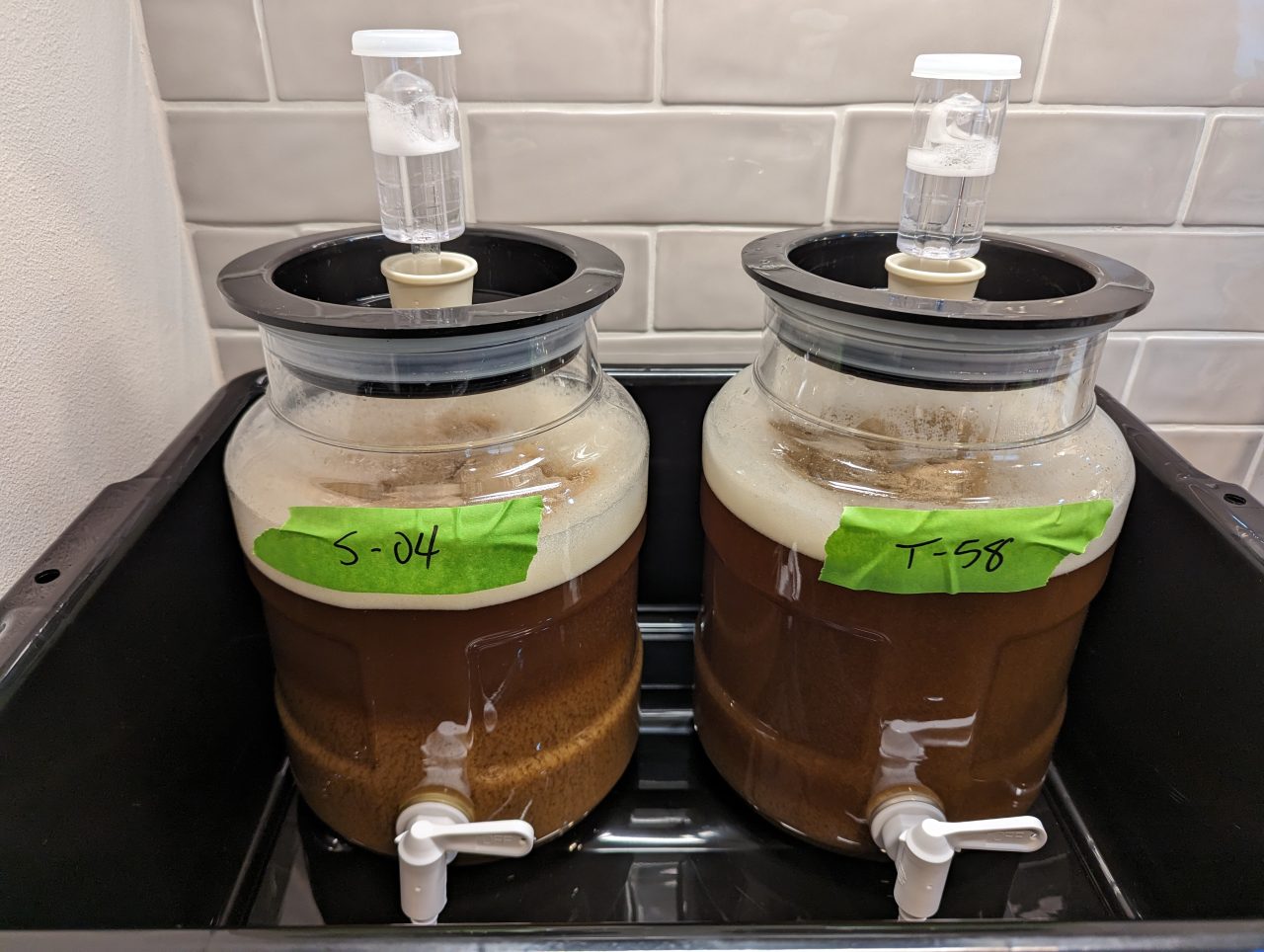 Photo of two small beer fermenters next to each other, with a green duct tape label on each. The label on the left fermenter is S-04 and the label on the right is T-58.
