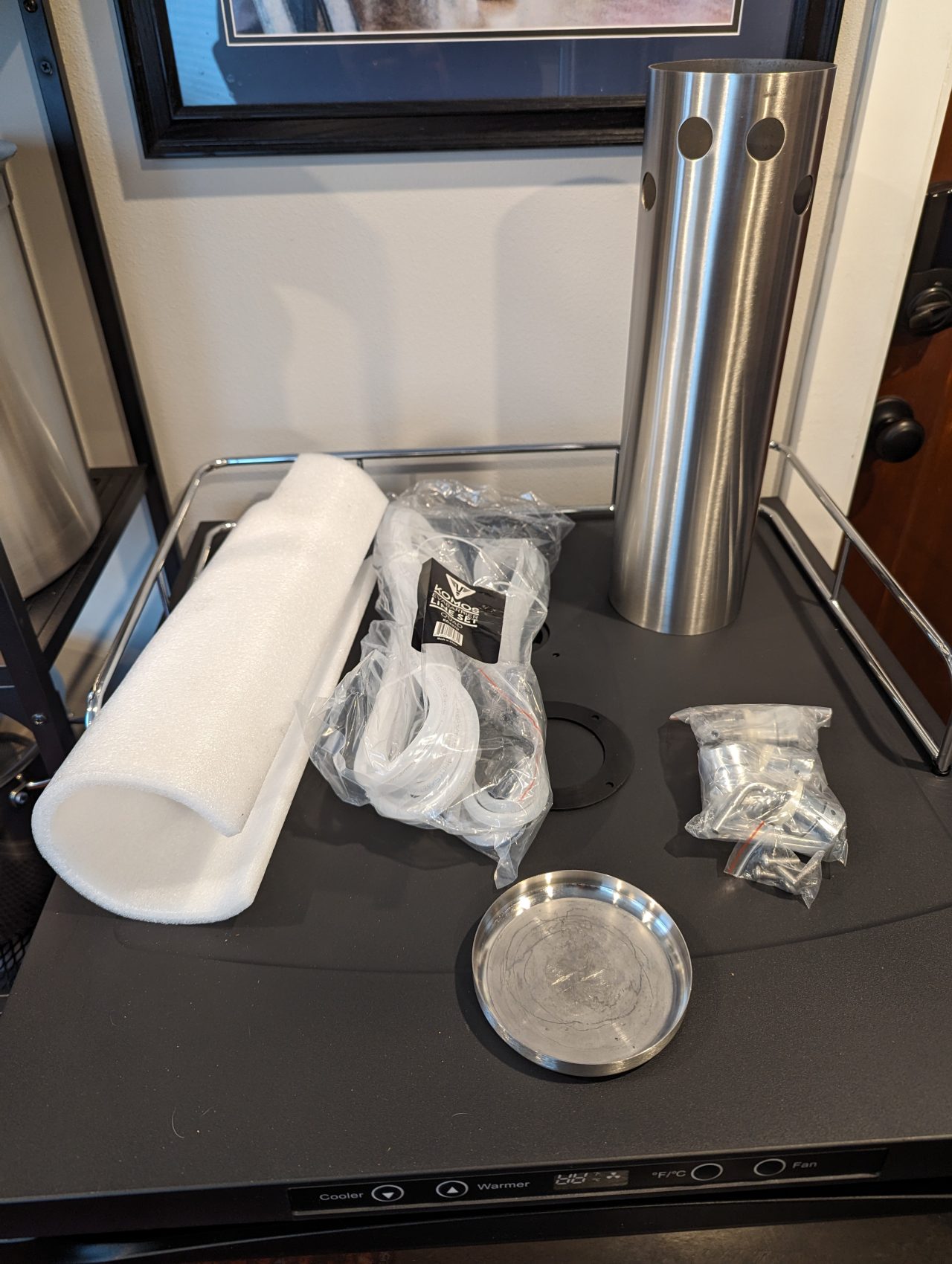 Photo of a stainless steel beer tap tower, various assembly parts, and a piece of foam insulation.