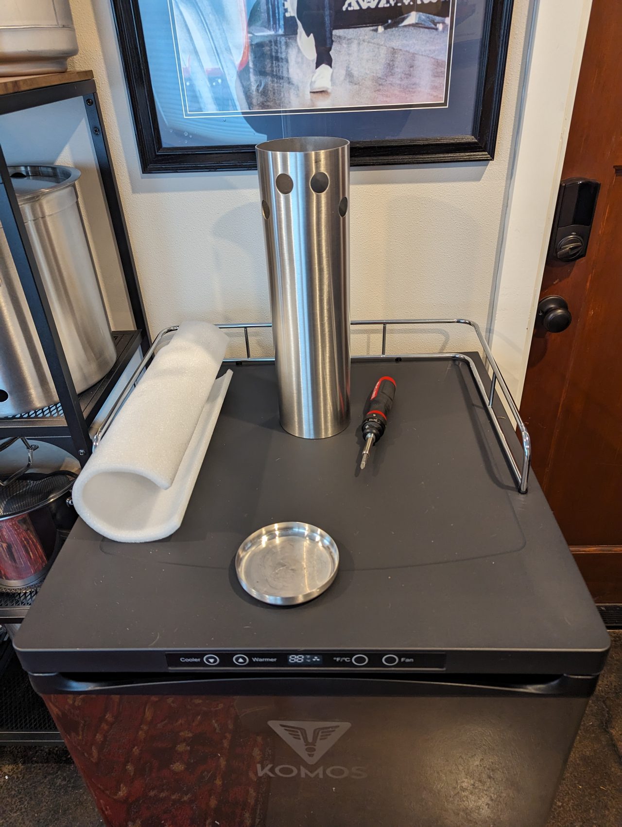 Photo of a beer tap tower installed on a kegerator with a screwdriver to the right, a piece of foam insulation to the left, and a stainless steel cap in front of the tower.
