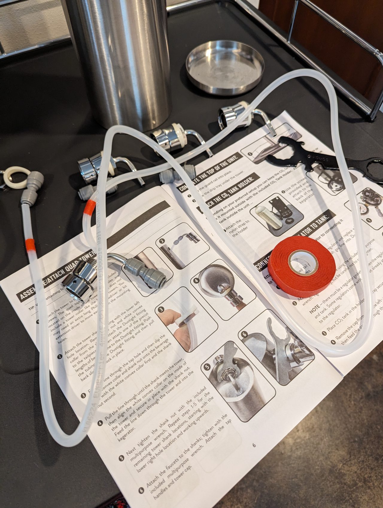 Photo of a piece of beer line, a kegerator assembly manual, and a small roll of red masking tape on top of a kegerator