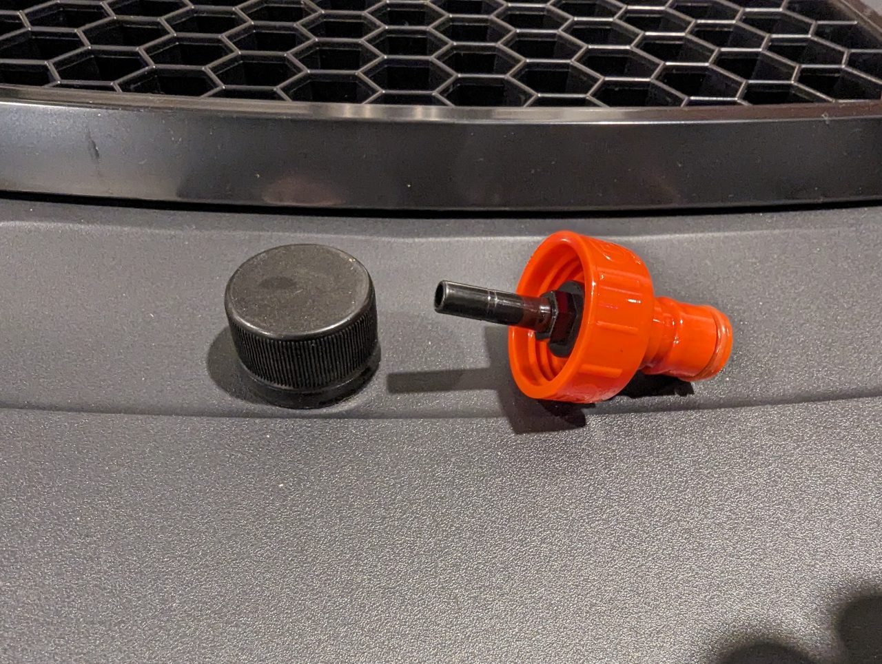 Photo of a plastic carbonation cap, which is a screw-on cap the size of a soda bottle cap that has a barb coming out one end, and has a ball lock fitting on the other end