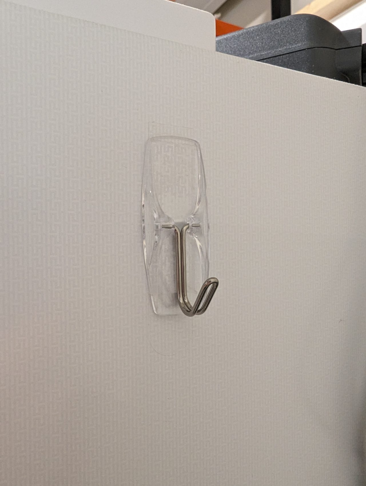 Photo of a small command strip hook mounted on the outside wall of an upright freezer