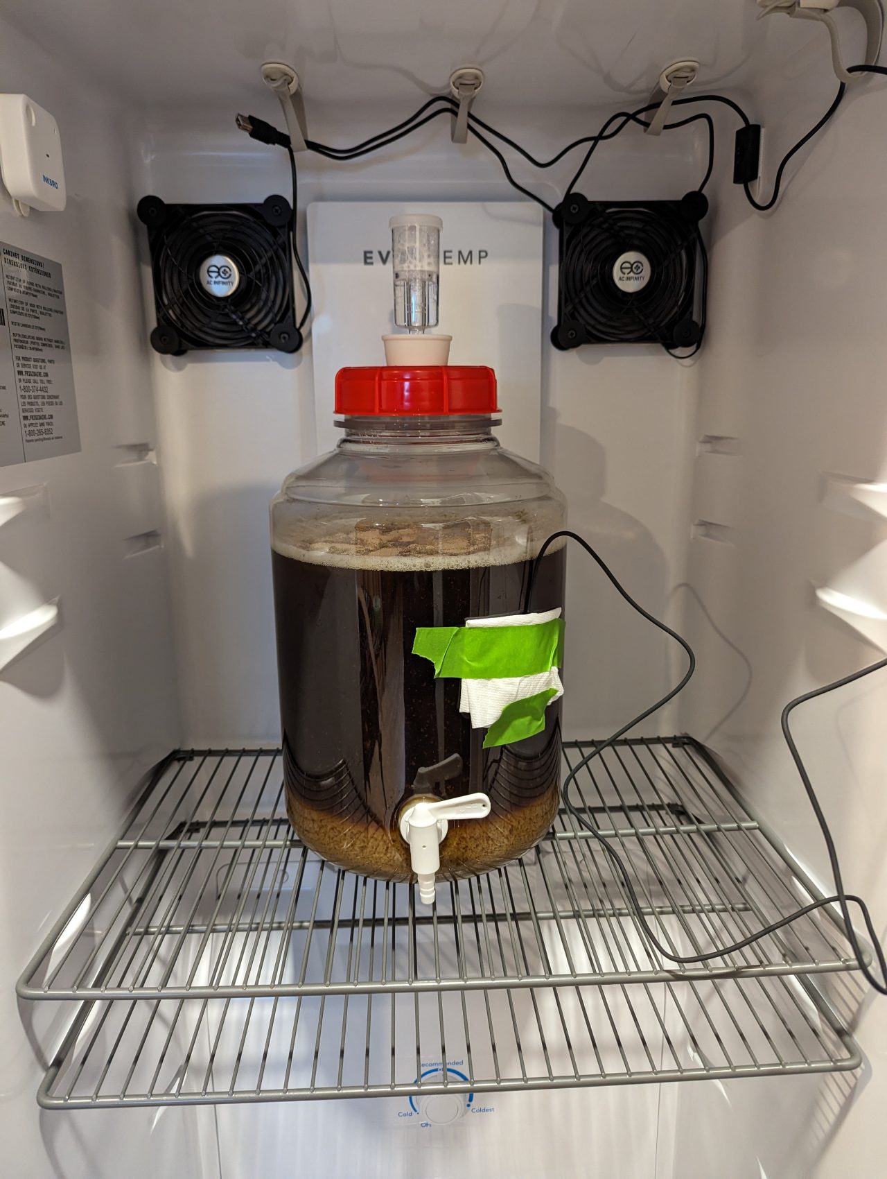 Photo of a plastic fermenter with a batch of beer inside it, and a temperature probe taped to the side underneath a folded paper towel